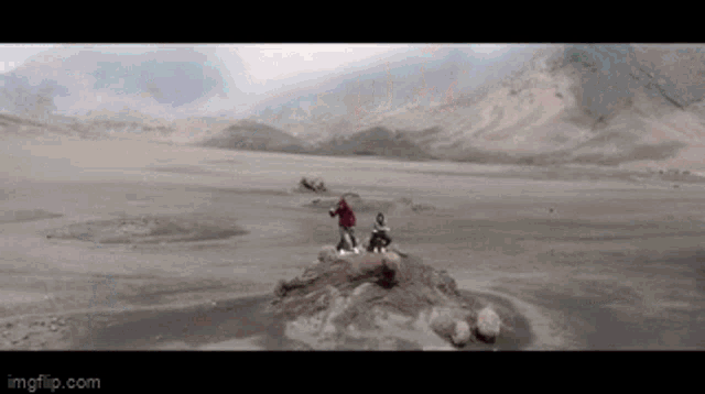 two people standing on a rock in the middle of a desert ..