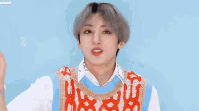 a young man with gray hair is wearing a white shirt and a red and blue vest .