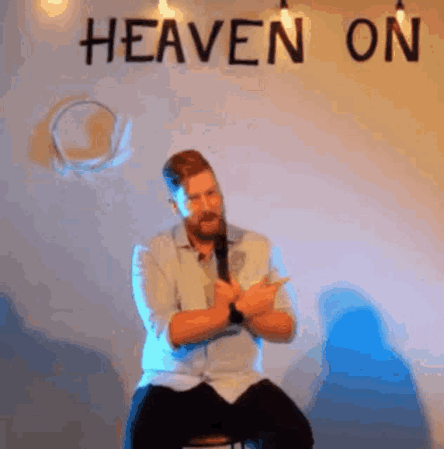 a man is sitting on a stool in front of a sign that says heaven on