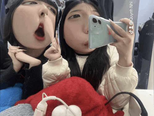 two girls are taking a selfie with a phone that says @quynh nhi on the bottom