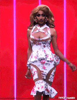 a drag queen is walking down the runway wearing a floral dress and earrings .