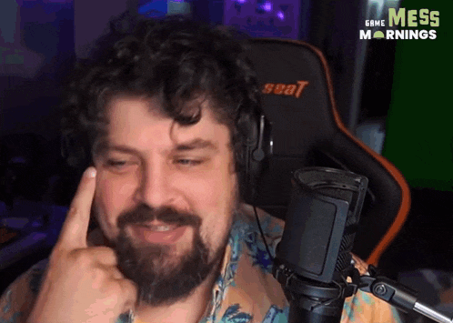 a man with a beard is sitting in front of a microphone wearing headphones and making a funny face .