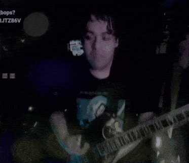 a man in a black shirt is playing a guitar in a dark room ..