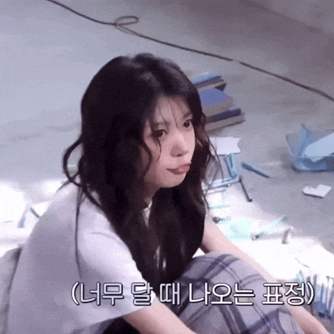 a girl is sitting on the floor with her tongue sticking out and korean writing on the bottom