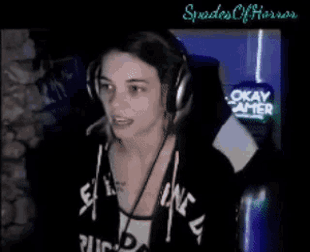 a woman wearing headphones is sitting in front of a sign that says " okay gamer "