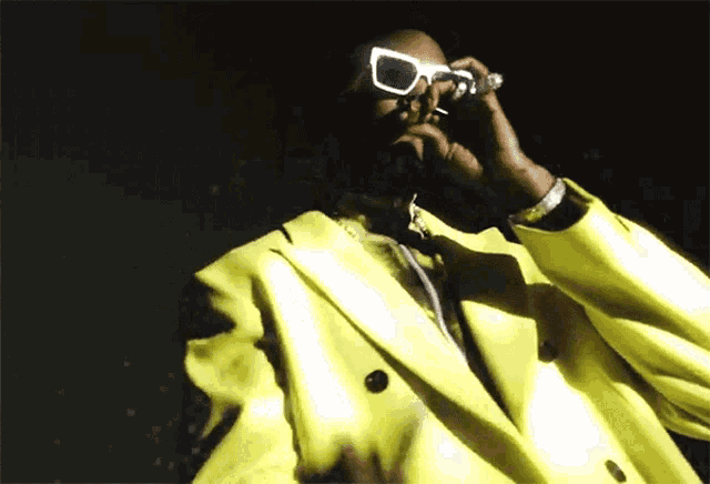 a man in a yellow suit and white sunglasses looks through a magnifying glass