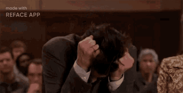 a man in a suit and tie is covering his face with his hands .