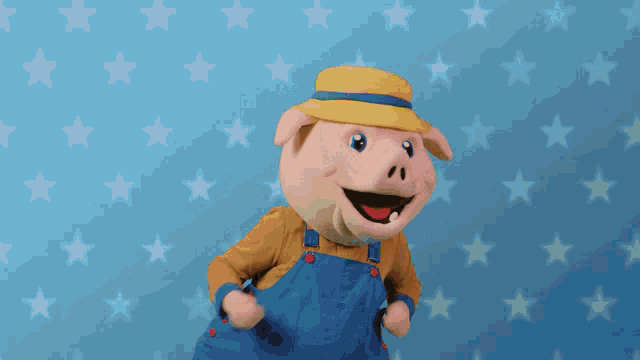 a pig mascot wearing blue overalls and a yellow hat stands in front of a blue background with stars