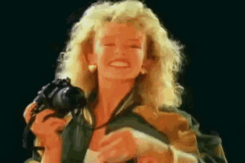 a woman with blonde hair is holding a camera in her hands and smiling .