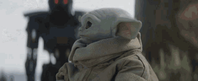 a baby yoda is sitting in front of a robot in a field .
