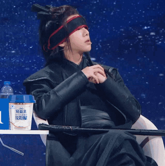 a man wearing a blindfold sits in a chair next to a container that says ' yogurt ' on it