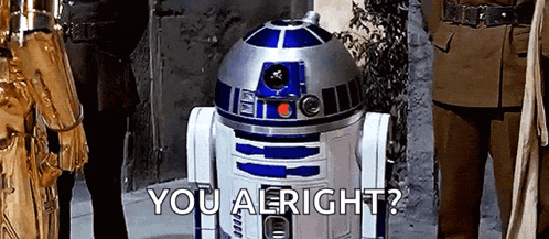 a r2d2 robot from star wars is standing in front of a group of people and asking if they are alright .
