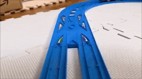 a blue toy train track is on a white mat .