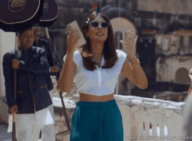 a woman wearing sunglasses and a crop top stands in front of a man holding an umbrella with the word karan on it