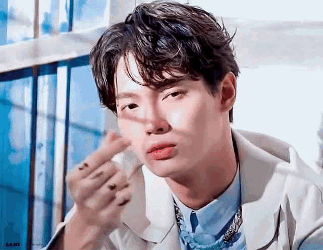 a young man wearing a white jacket and a blue shirt is making a heart shape with his finger .