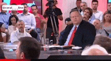 a man in a suit and tie is sitting at a table in front of a group of people .