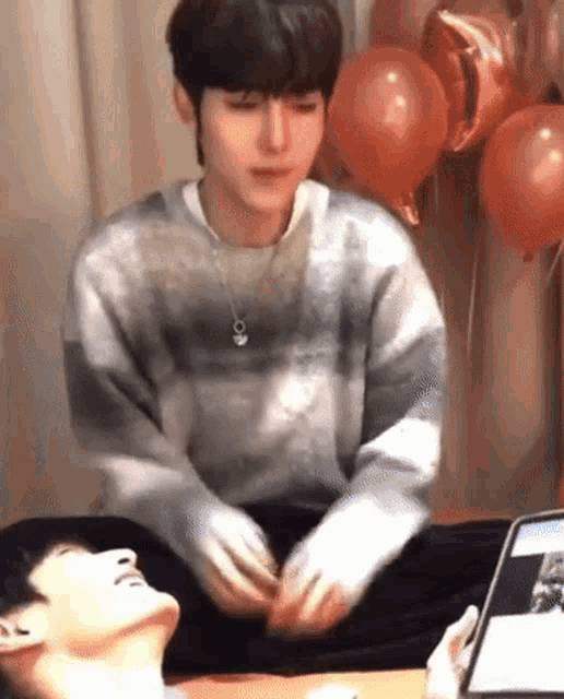 a man is sitting at a table with balloons in the background and playing with another man 's head .