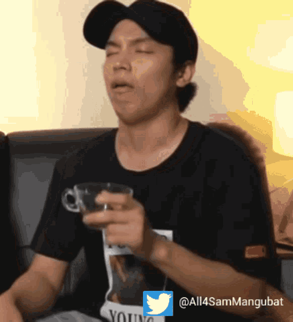 a man wearing a black shirt that says young holds a cup