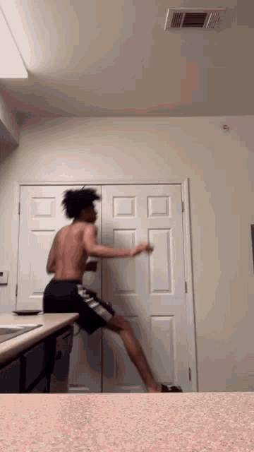 a shirtless man in black shorts is standing on a counter in front of a white door .