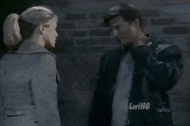 a man and a woman are standing next to each other in front of a brick wall with lorihq written on the bottom