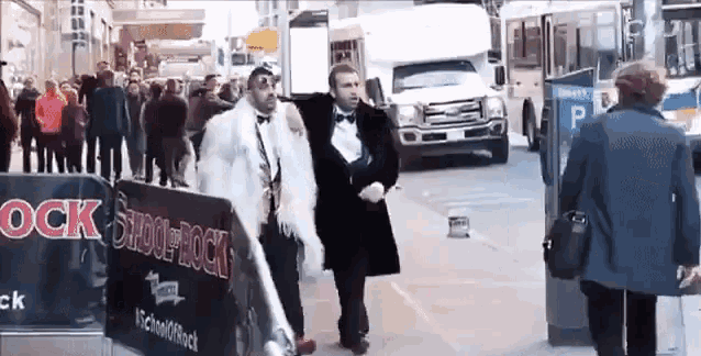 a man in a tuxedo walks down a street with a sign that says saddle rock