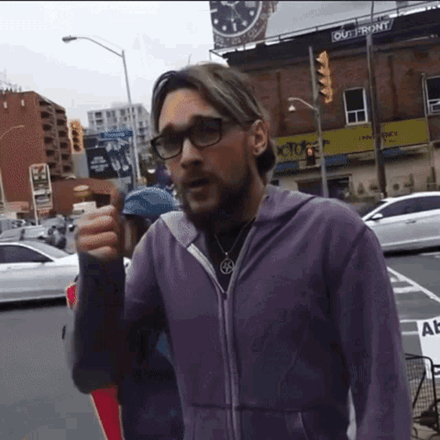 a man in a purple jacket is giving a thumbs up in front of a building that says out front