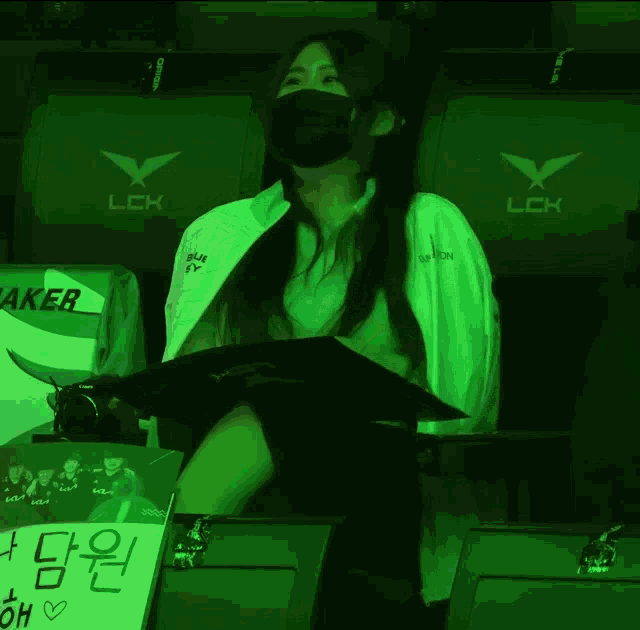 a woman wearing a mask sits in front of a lck chair