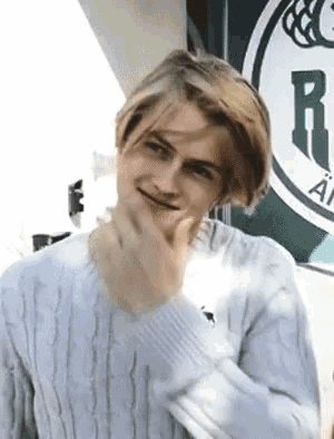a young man in a white sweater is making a funny face while standing in front of a sign .