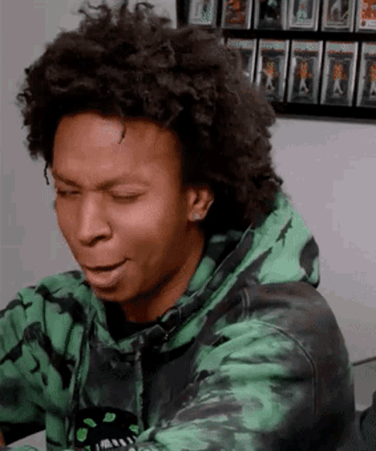 a man wearing a green and black tie dye hoodie looks down with his eyes closed