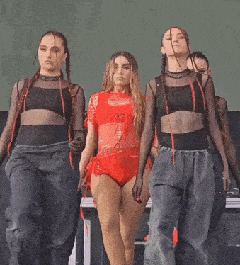 a woman in a red bodysuit is standing between two dancers .