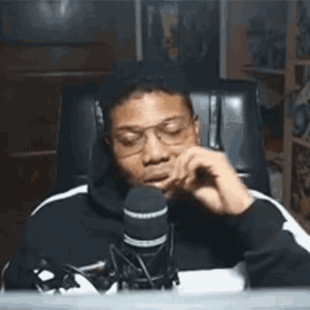 a man wearing glasses is sitting in front of a microphone and talking into it .