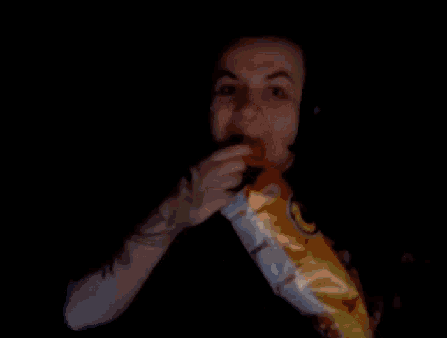 a man is eating a bag of cheetos in the dark .