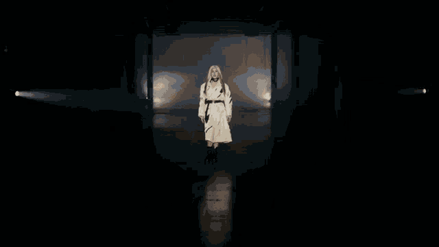 a woman in a white coat is standing in the dark