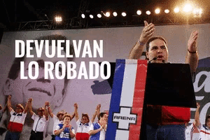 a man stands at a podium with the words devuelvan lo robado on the bottom