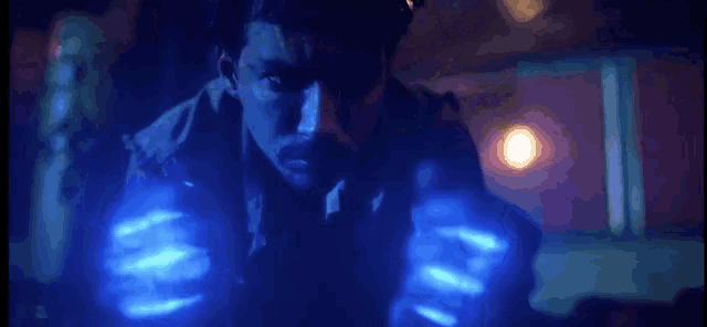 a man in a dark room with a blue light coming out of his hands