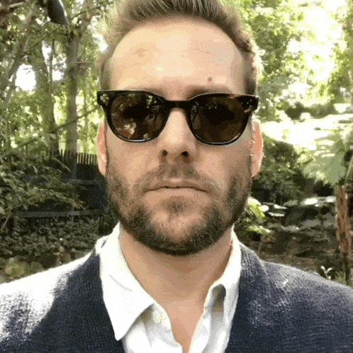 a man with a beard is wearing sunglasses and a blue sweater