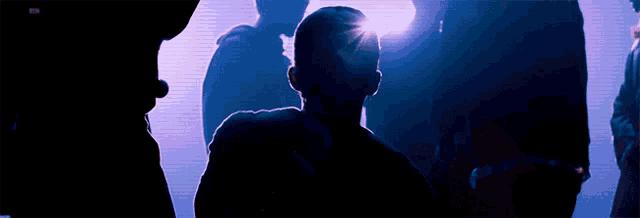 a group of people standing in a dark room with a purple light shining on them