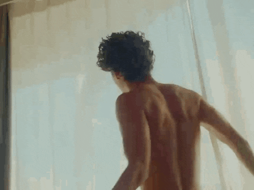 a shirtless man is standing in front of a window with his hand in his hair .