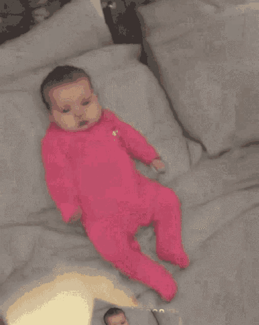 a baby in a pink outfit is laying on a bed with pillows