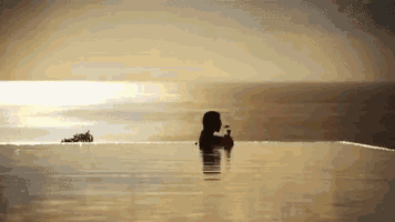 a woman is sitting in a swimming pool with a drink in her hand at sunset