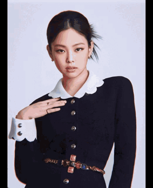 a woman wearing a black dress with a white collar and cuffs has her hand on her chest