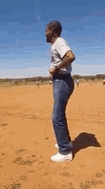 a man is standing on a dirt field with his hands in his pockets .