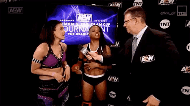 a man in a suit is talking to two women wrestlers .