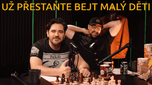 two men are sitting at a table with a chess board and the words uz prestante bejt maly deti