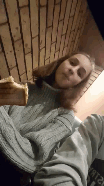 a girl in a sweater is holding a piece of food