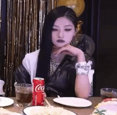 a woman is sitting at a table with a can of coca-cola and plates of food .