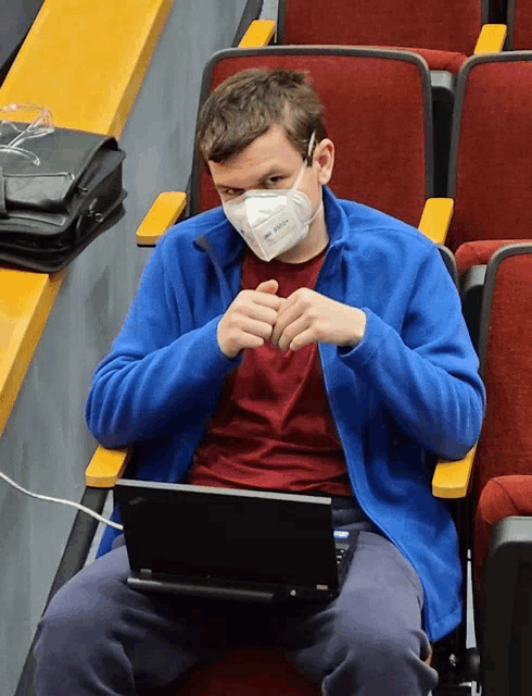 a man wearing a kn95 mask sits in a chair with a laptop