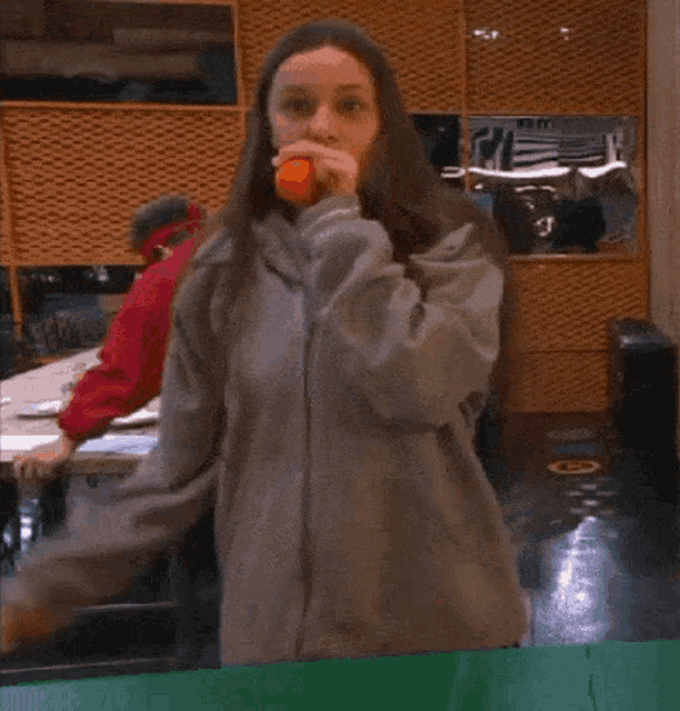 a woman in a grey sweatshirt is holding an orange in her hand
