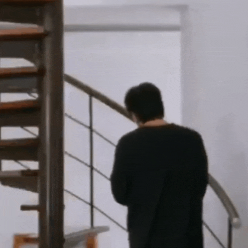 a man in a black shirt is standing on a spiral staircase looking down .