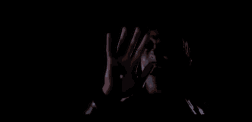 a person with a bloody hand covering their face in the dark